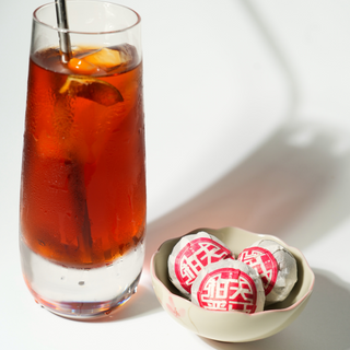 Glass of iced tea with a bowl of tea oranges on a white background