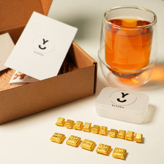 Yustea tea packaging with gold tea resins and a glass of tea on a white surface.