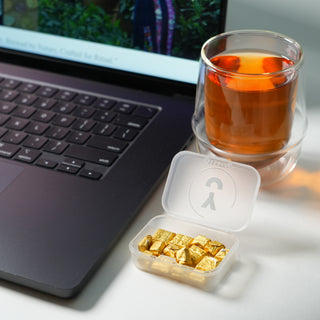 Laptop with a glass of tea and container of tea resins on a desk