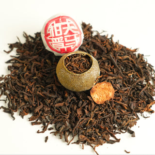 Tea leaves with a tea ball and a small round object on a white background