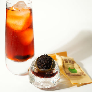 Glass of iced tea with a small container of tea leaves and tea orange on a white background