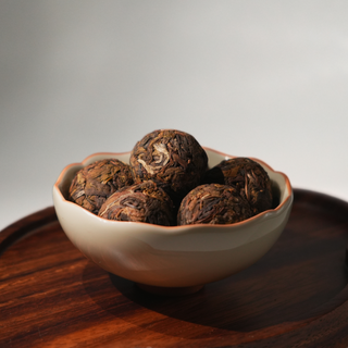 Bowl of dark brown tea balls on a wooden tray with a gray background