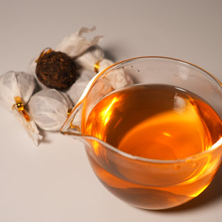 he beautiful golden-amber tea liquor brewed from Yustea's Pu'er Dragon Balls, shown in a glass fairness pitcher with the tea balls in the background.