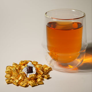 Glass of amber liquid with gold tea bags on a light background