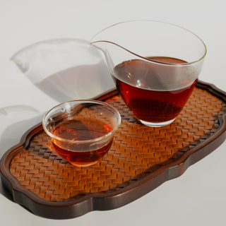 A glass fairness pitcher (gong dao bei) and a small tasting cup filled with the rich, amber brew of Yustea's Xiaoqinggan Green Mandarin Pu'er tea.