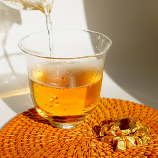 The process of brewing a perfect cup of tea, with hot water being poured into a glass over a Yustea tea cube on a woven placemat.