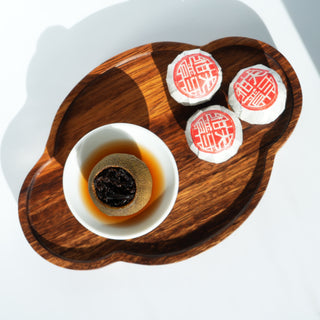 A glass fairness pitcher (gong dao bei) and a small tasting cup filled with the rich, amber brew of Yustea's Xiaoqinggan Green Mandarin Pu'er tea.