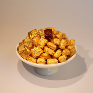 A white cup filled with golden-brown tea resin pieces, with a small piece of dark tea resin on top, placed on a light background.