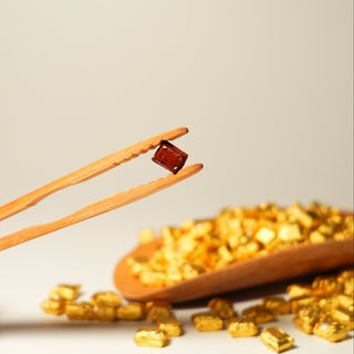 Wooden chopsticks holding a small red object over a pile of gold-colored stones on a beige background